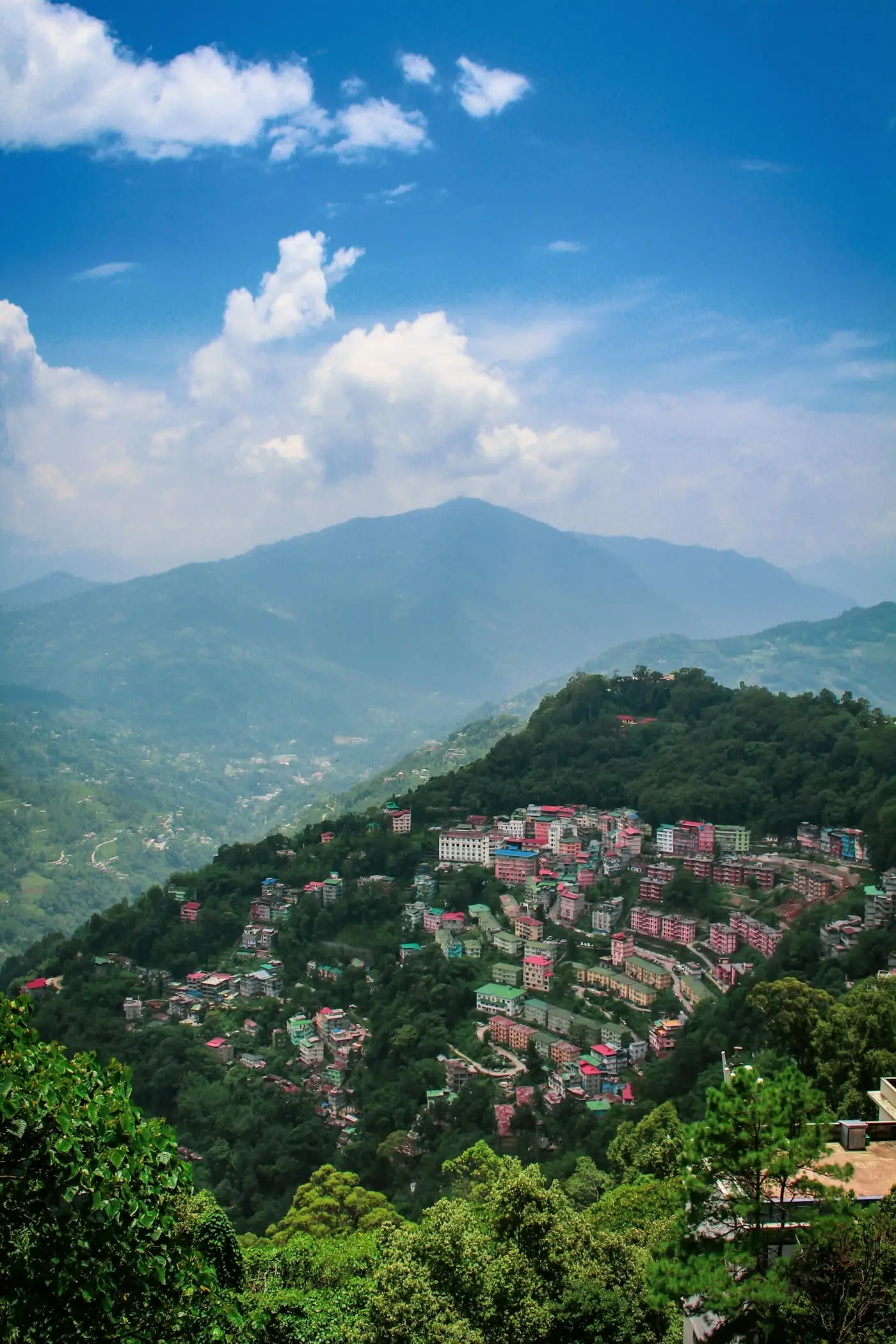 Houses clinging to a green Sikkim hillside under a blue sky