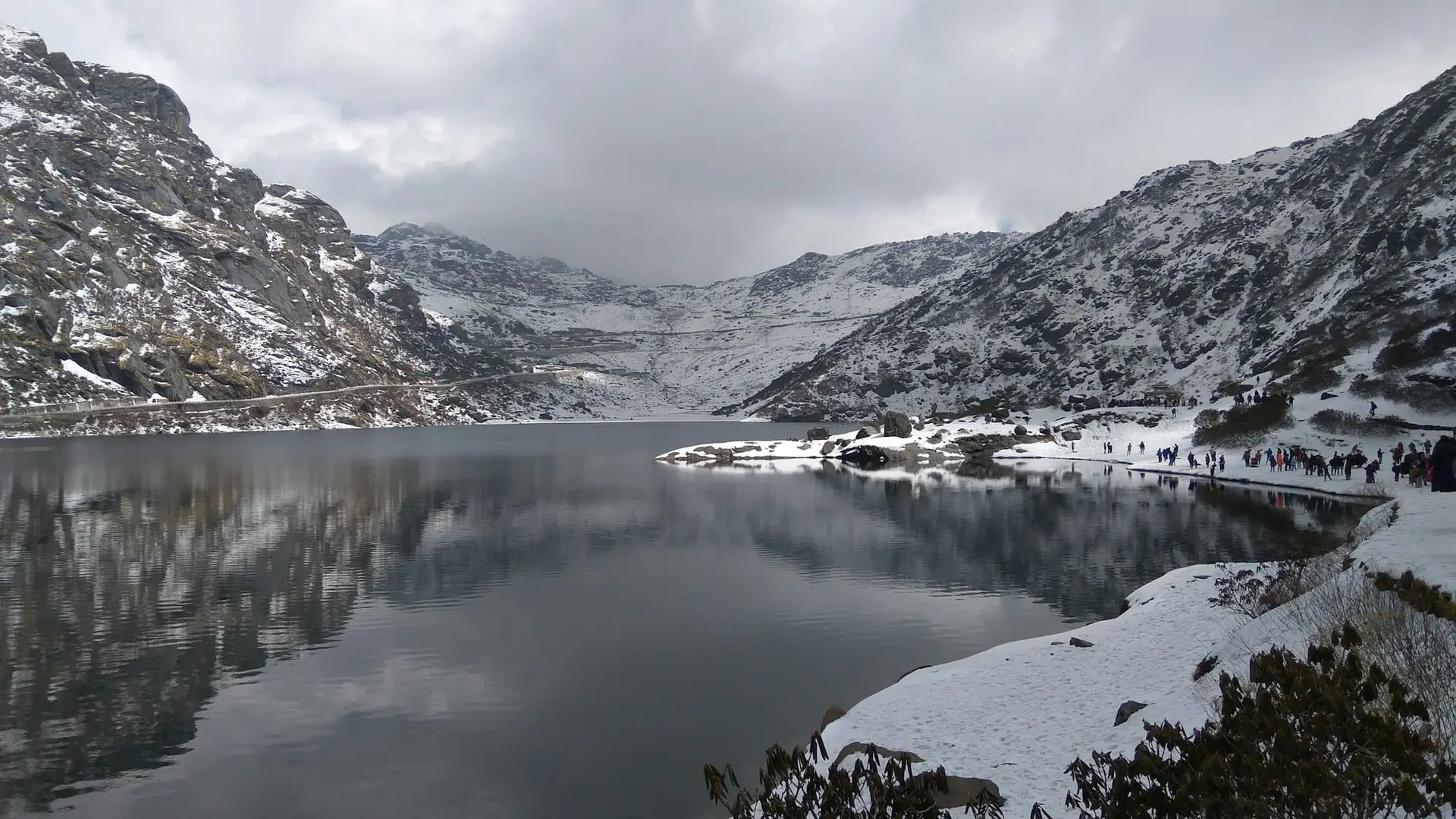 Tsomgo Lake lying still between snow-dusted slopes